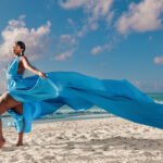 A milestone portrait on the beach in Riviera Maya, featuring a subject in a colorful flying dress with fabric billowing outward in the sea wind.