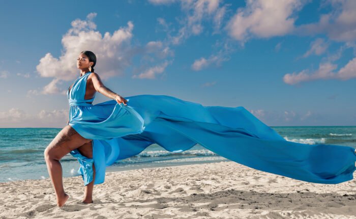 A milestone portrait on the beach in Riviera Maya, featuring a subject in a colorful flying dress with fabric billowing outward in the sea wind.