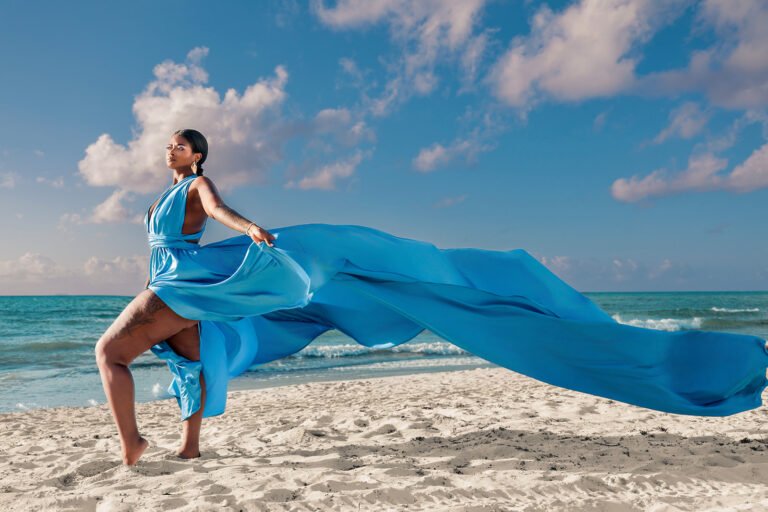 TINY A milestone portrait on the beach in Riviera Maya, featuring a subject in a colorful flying dress with fabric billowing outward in the sea wind.
