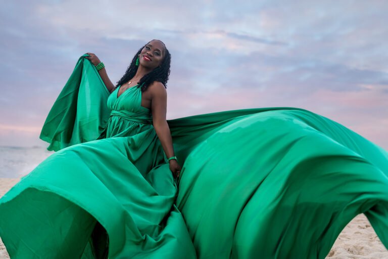 THERESE Full-length portrait of a birthday participant on the Riviera Maya coastline, wrapped in a shimmering emerald green dress with a long train trailing over the white sand.
